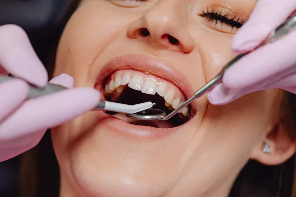 Smiling woman at dentist with tools for dental exam, highlighting dental care.