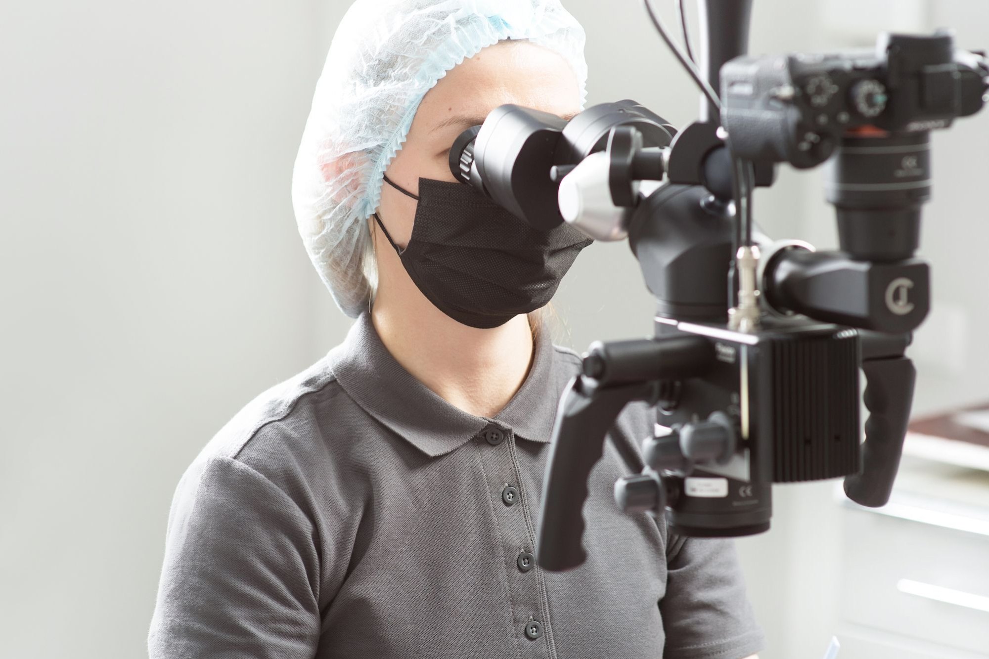 A dentist wearing a mask uses a microscope in a dental clinic while treating a patient.